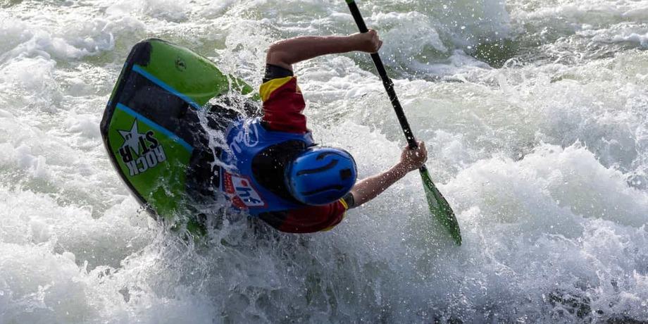 Kajakfahrer manoeuvriert durch hohe Wellen in einem Wildwasserbereich, Paddel in der Hand, Kopf nach unten geneigt.