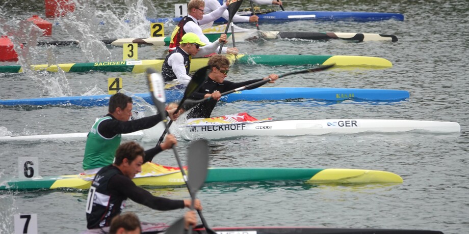 Rennszenen mit mehreren Kanuten in Booten, die in einer Wasserstrecke paddeln, spritzen Wassertropfen auf.