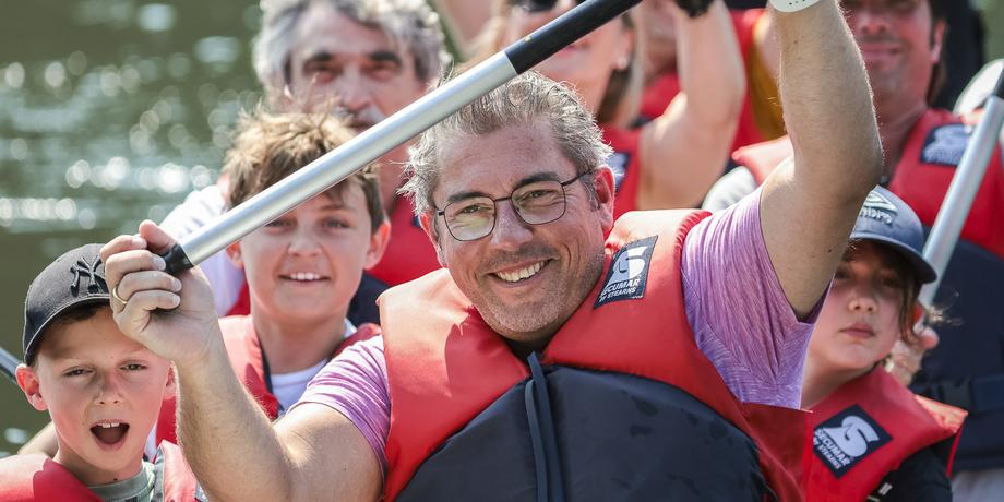 Gruppe von Menschen in roten Rettungswesten, die beim Kanufahren lachen und Paddel in die Luft halten.
