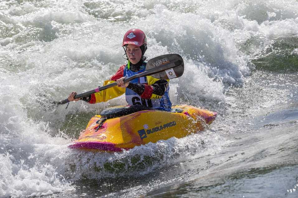 Kind paddelt mit einem Kanu durch aufgewühlte Wellen, spritzendes Wasser um ihn herum.