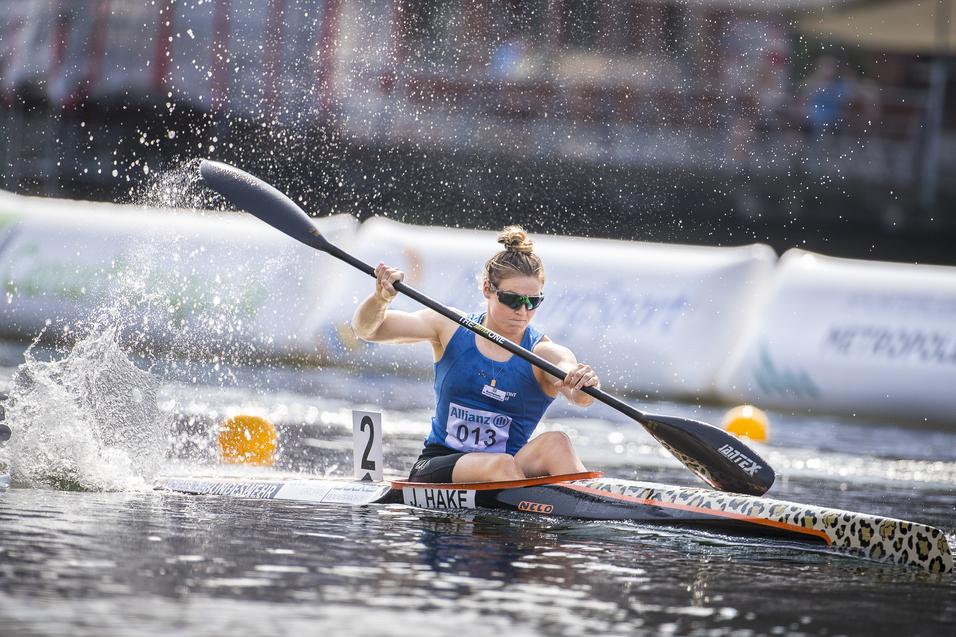 Paddlerin in einem Kanu steuert mit einem Paddel durch glattes Wasser, spritzt Wasser aufspritzt, während sie an einer Boje vorbeifährt.