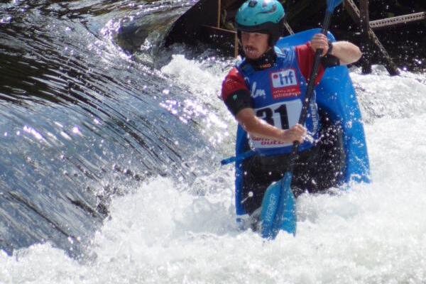 Kajakfahrer mit Helm und Paddel bezwingt spritzige Strömungen an einer Wasserstelle.