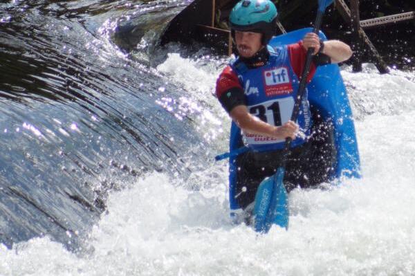 Kajakfahrer mit Helm und Paddel bezwingt spritzige Strömungen an einer Wasserstelle.