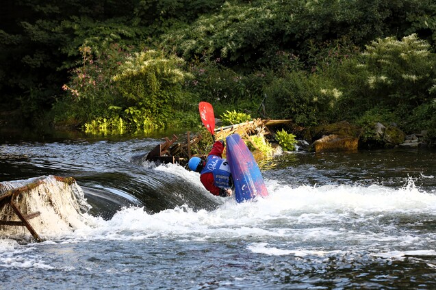 Kajakfahrer in einem türkisfarbenen Kajak, der über eine kleine Wasser oberfläche fährt und spritzende Wellen erzeugt.