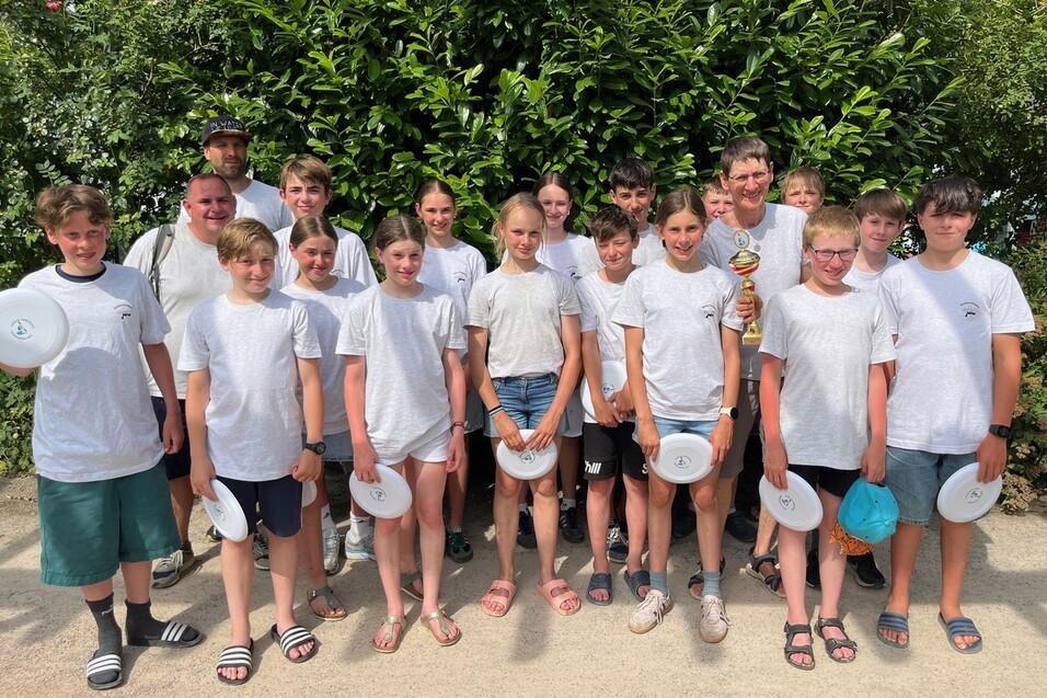 Gruppenfoto von Kindern und Jugendlichen in grauen T-Shirts, die Frisbees halten, mit einem Pokal in der Mitte.