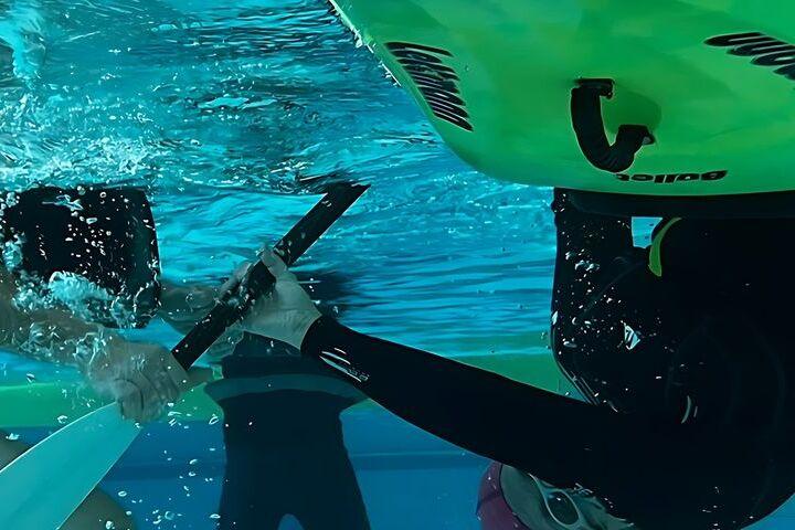 Zwei Personen in Neoprenanzügen üben unter Wasser Kanu-Rettungstechniken in einem Schwimmbecken.
