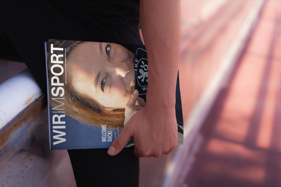 Nahaufnahme einer Person, die ein Sportmagazin mit einem Gesichtsausdruck darauf in der Hand hält.