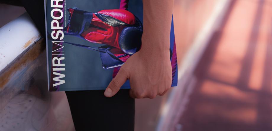 Nahaufnahme einer Hand, die eine Sportzeitschrift mit Boxhandschuhen auf dem Cover hält, auf einer Laufbahn sitzend.